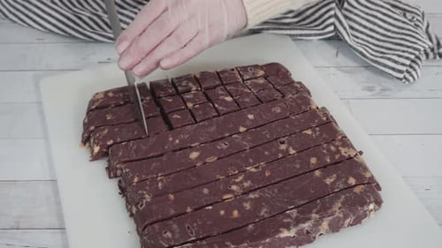 Schritt für Schritt. Hausgemachten Macadamia-Fudge auf einem weißen Schneidebrett schneiden.