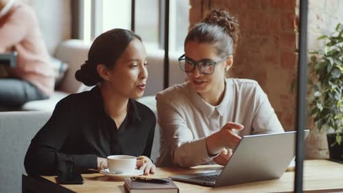 Dos jóvenes empresarias usan una computadora portátil y hablan en un café