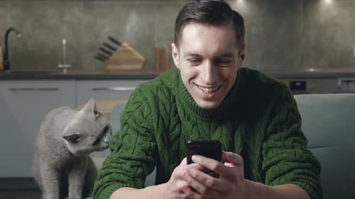 Man Using Mobile Phone with Cat Indoors