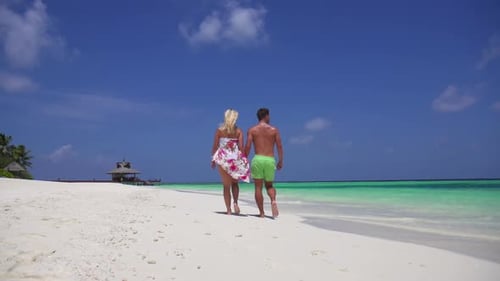 A couple walks on the beach holding hands at a tropical island resort hotel