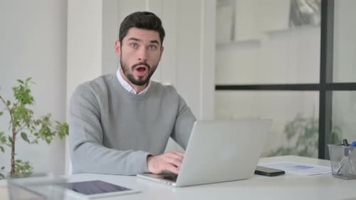 Young Man Feeling Shocked While Using Laptop in Office