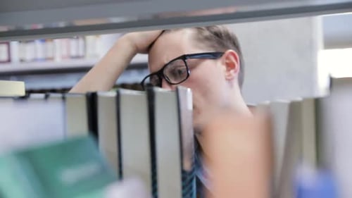 College Library. Male Student Searching For Book On Bookshelves