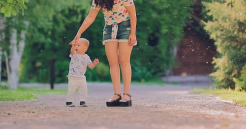 Pretty Baby Stands with Her Mother By the Handle for a Walk in the Summer