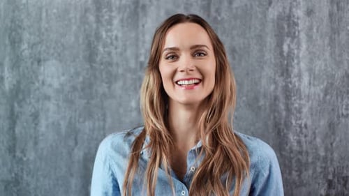 Smiling Woman in Blue Shirt Against Gray Backdrop