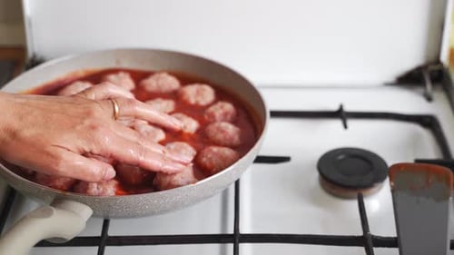 Adding Raw Meatballs to Tomato Sauce on Stove