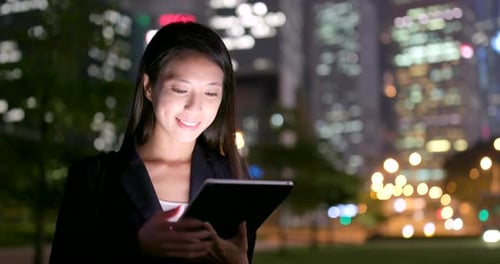 Woman Uses Tablet at Night in City Park
