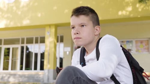A Caucasian Teenage Boy Thinks About Something As He Sits in Front of School Closeup