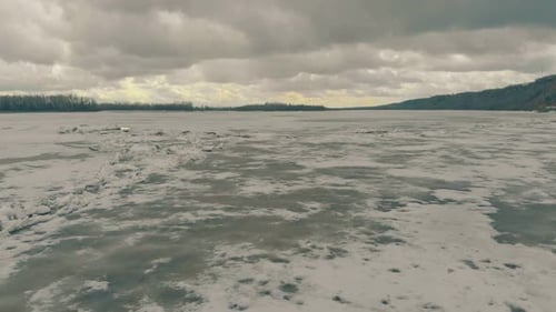 Aerial Motion Over Frozen River with Snow Under Cloudy Sky