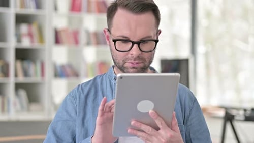 Man Using Tablet Device Indoors Near Bookshelf
