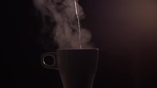 Hot boiled water is poured into a white ceramic cup or mug on black background with light