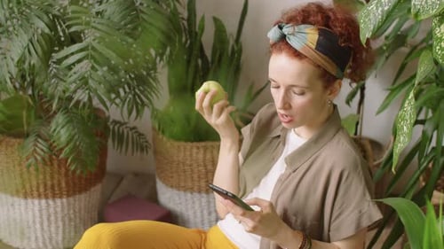 Woman Eating Apple and Using Mobile Phone at Home