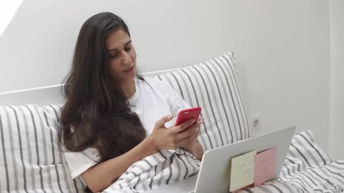 Woman in Bed Using Phone and Laptop