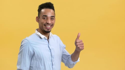 Young Adult Smiling with Thumbs Up on Yellow