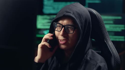 Hooded Hacker Answering Phone Call in Dark Room