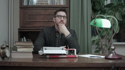 Nachdenklicher Schriftsteller sitzt vor Schreibmaschine und wartet auf Inspiration für sein neues Buch