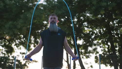 Handsome Middle Aged Man with Long Gray Beard Jumping a Rope During Sunsise Close Up Shot Slow
