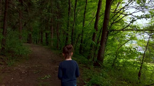 Nahaufnahme eines kleinen Mädchens, das allein im dunklen, gruseligen Wald auf einem Fußweg spaziert