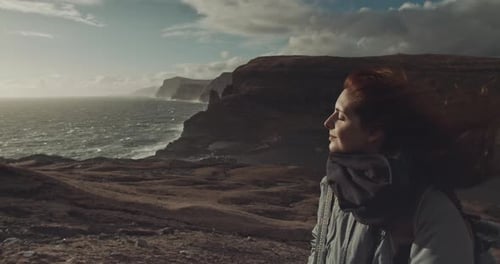 Woman Stands on Windy Coastline Cliffside