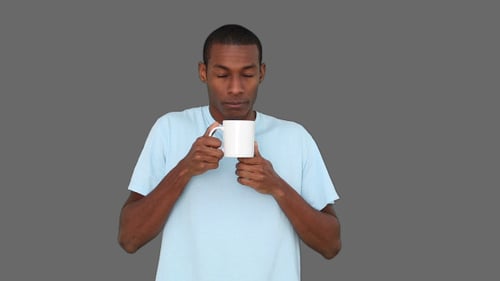 Young Man Enjoys Coffee or Tea from White Mug