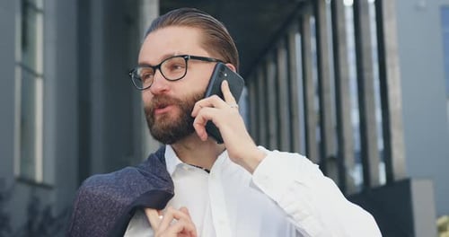 Office Worker in glasses which has positive phone conversation outdoors during time break