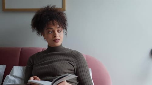 Young Woman Lying And Relaxing On Bed At Home Reading Book