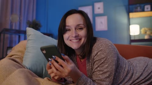 Woman Relaxing on Couch Using Phone at Night