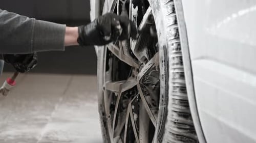 Joven que usa un cepillo para limpiar la superficie del borde de un automóvil en Auto Wash
