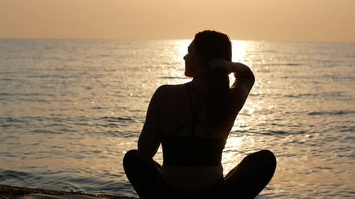 Une femme yogi est assise en position de lotus au bord de la mer et regarde l'aube du soleil.
