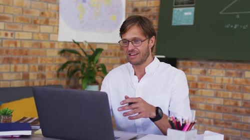 Caucasian male teacher teaching on videocall on laptop in the classroom at school