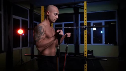 Muscular Man Curls Resistance Bands in Dark Gym