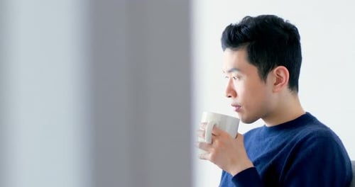 Young Adult Drinks from Mug and Uses Tablet