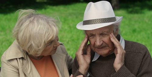 Senior Man with Headache Comforted by Wife in Park