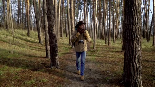 Backpacker with Camera Walks Along a Trail in the Forest