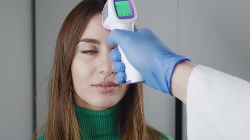 Temperature Measurement By Electronic Infrared Thermometer for a Young Woman in Green Sweater