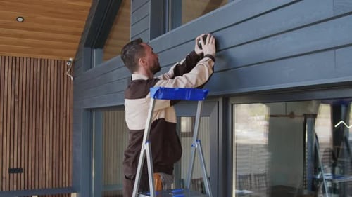 Man Installing Security Camera on House Exterior