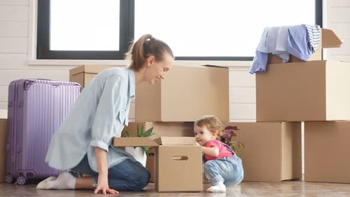 Kleines Kind schaut in Box. Hintergrund: Umzugskisten und Anzug.