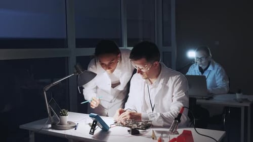 Elektronikingenieure gemischter Rassen in weißen Kitteln arbeiten mit Multimetertester am Motherboard