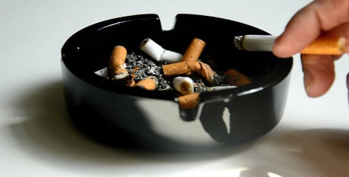 Hand Ashing Cigarette into Full Ashtray