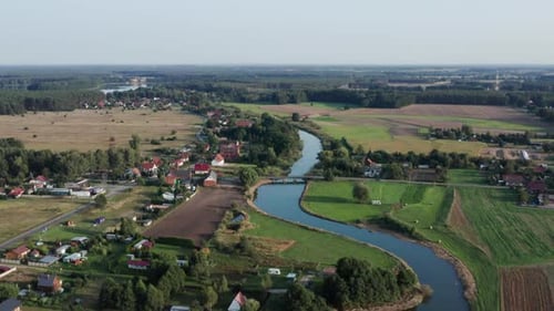 Toma aérea rural de un río curvilíneo con un puente de madera, que corre por un pequeño pueblo agrícola. Lago vi