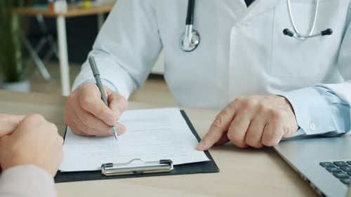Close-up of Male Doctor Filling in Medical Chart Talking To Female Patient in Office