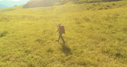 Flight Over Backpack Hiking Tourist Walking Across Green Mountain Field. Huge Rural Valley at Summer