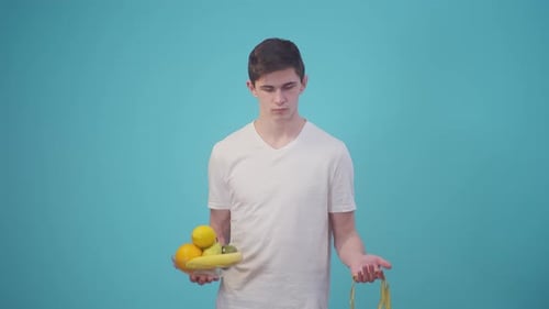 Man in a White Tshirt Holds Fruit and a Meter Ribbon on Blue Background in the Studio