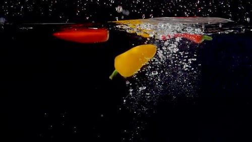 Colorful Peppers Splashing Into Water on Black