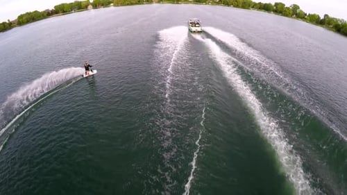 Aerial birds-eye drone view of a man wakeboarding behind a boat.