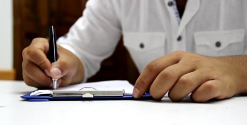 Adult writes on a clipboard with black pen