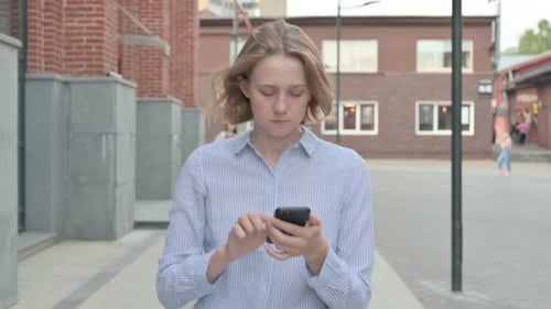 Woman Using Smartphone While Walking in Street
