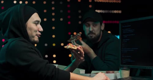 Young Adults Eating Pizza at Computer Workstation at Night