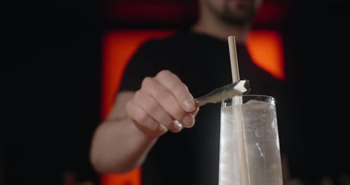 Barkeeper steckt den Strohhalm mit Eiswürfeln und Sodawasser in Zeitlupe Limonade in den Cocktail