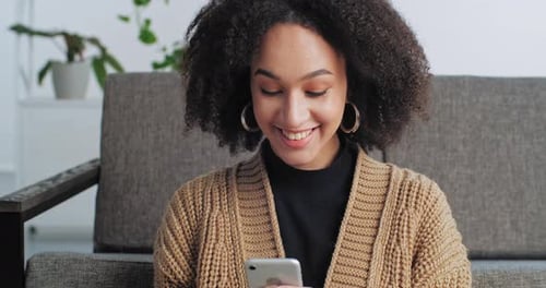 Woman Uses Smartphone Smiling Sitting on Sofa Indoors