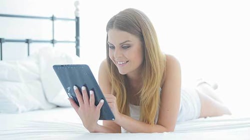 Smiling Girl Relaxing On Her Bed With A Tablet-pc